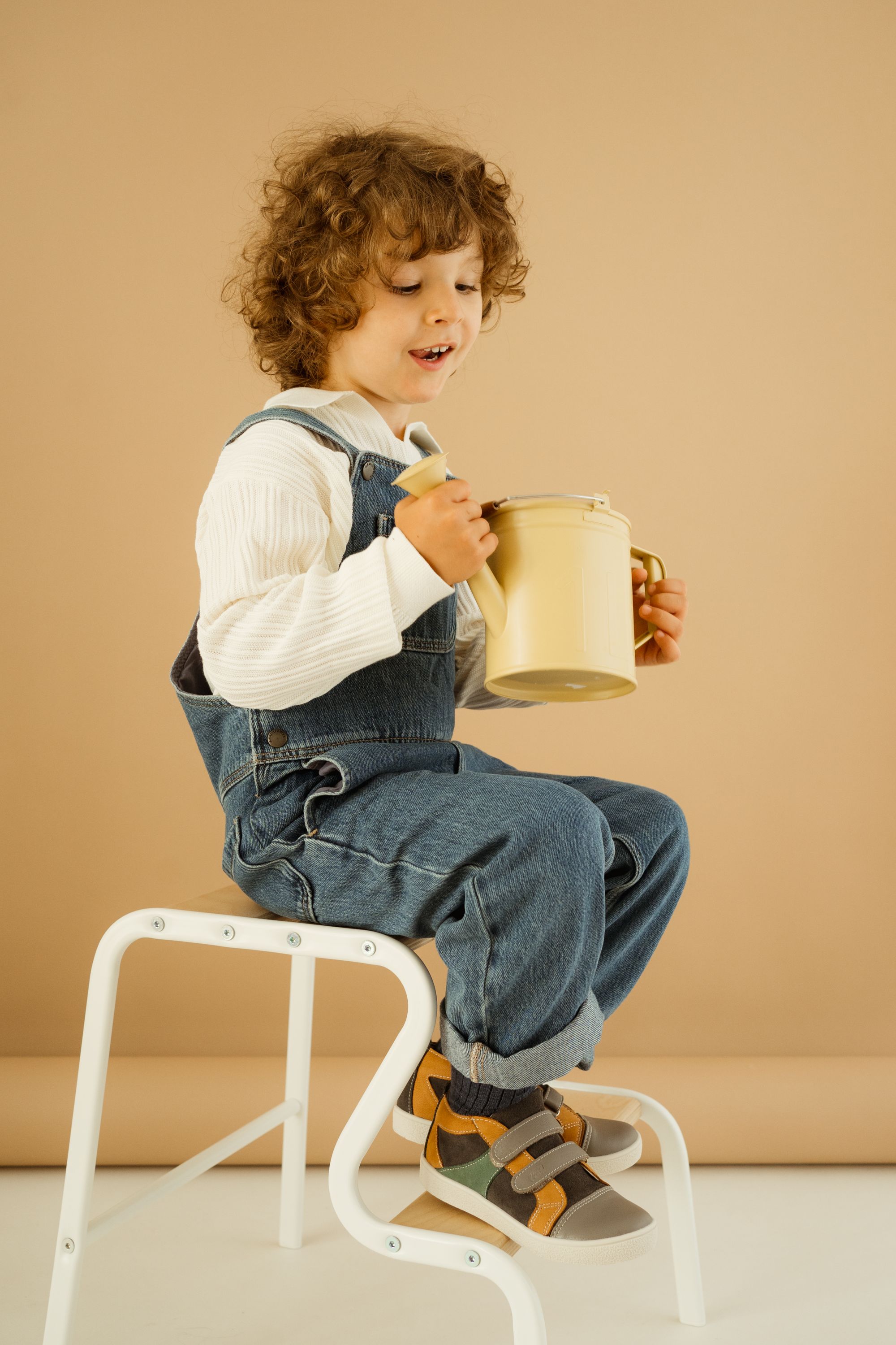 Dziecko siedzi na białym krzesełku i trzyma beżową konewkę 