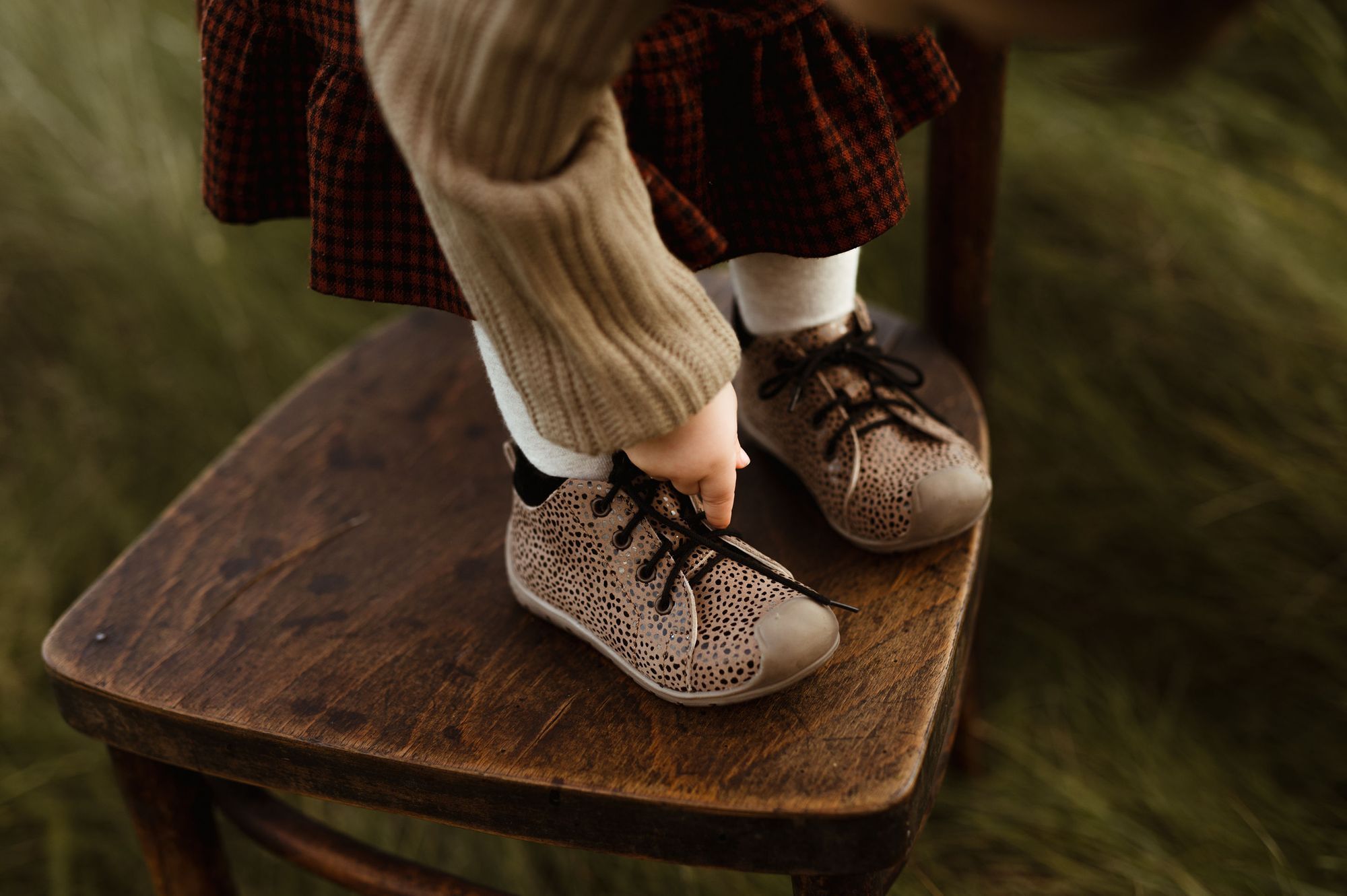 Dziecko stoi na brązowym drewnianym krześle w bucikach Emel