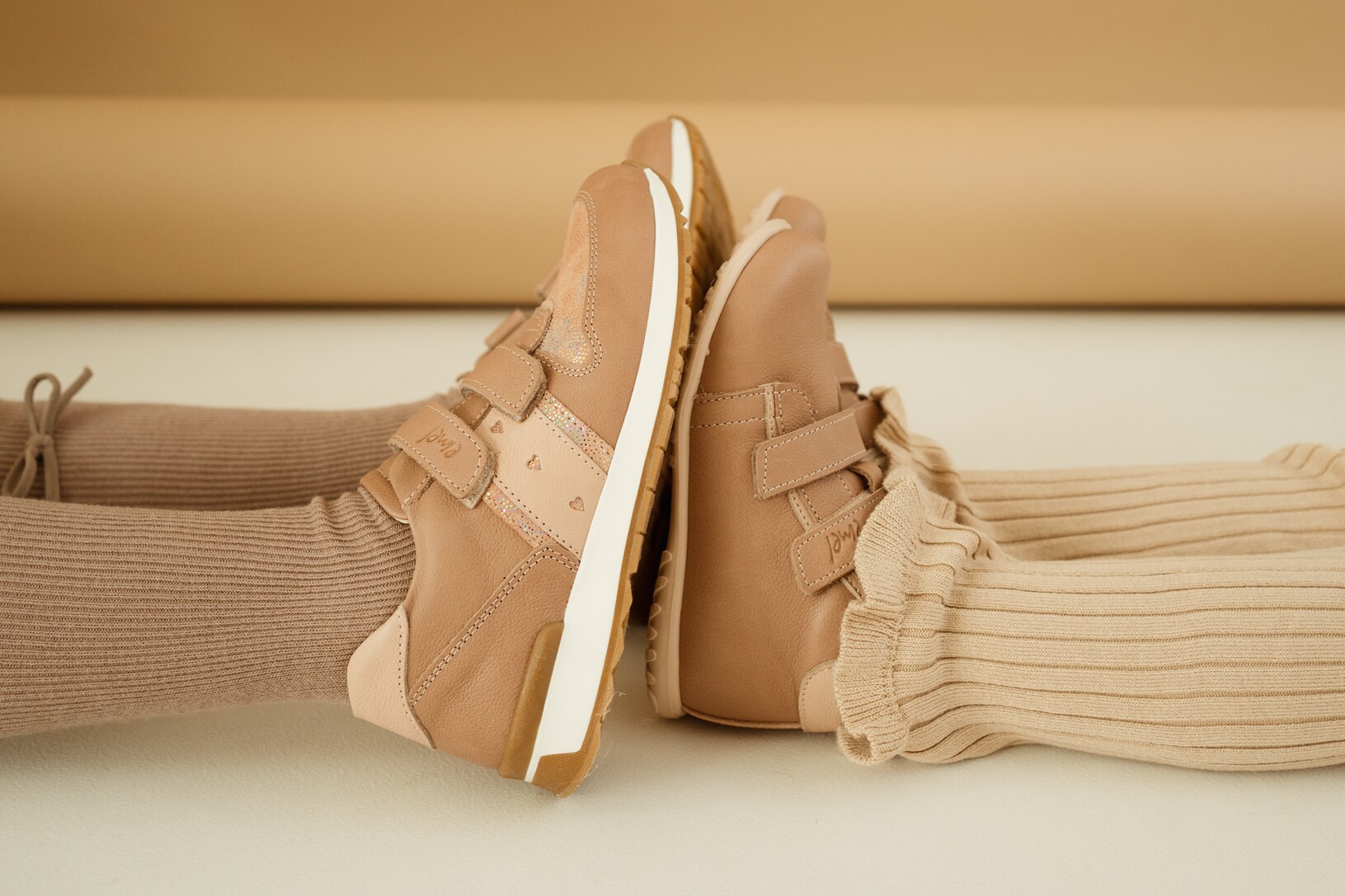 Skórzane ręcznie robione trampki dziecięce Emel – zbliżenie na stykające się podeszwy dwóch dziewczynek siedzących na podłodze, wysokiej jakości obuwie z naturalnej skóry.