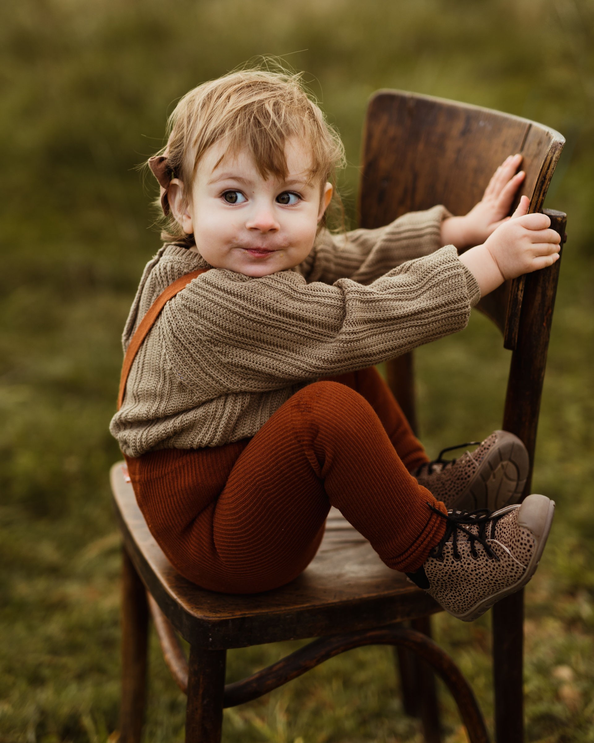 Mała dziewczynka siedzi na świeżym powietrzu, mając na nogach ręcznie wykonane buciki Roczki Emel z naturalnej skóry.