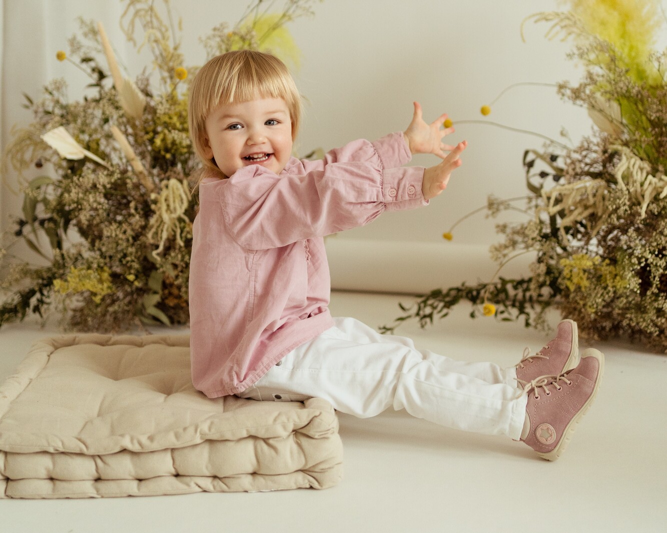 Roześmiana mała dziewczynka radośnie bawi się w różowych trzewikach Roczki firmy Emel wykonanych z miękkiej skóry welurowej.