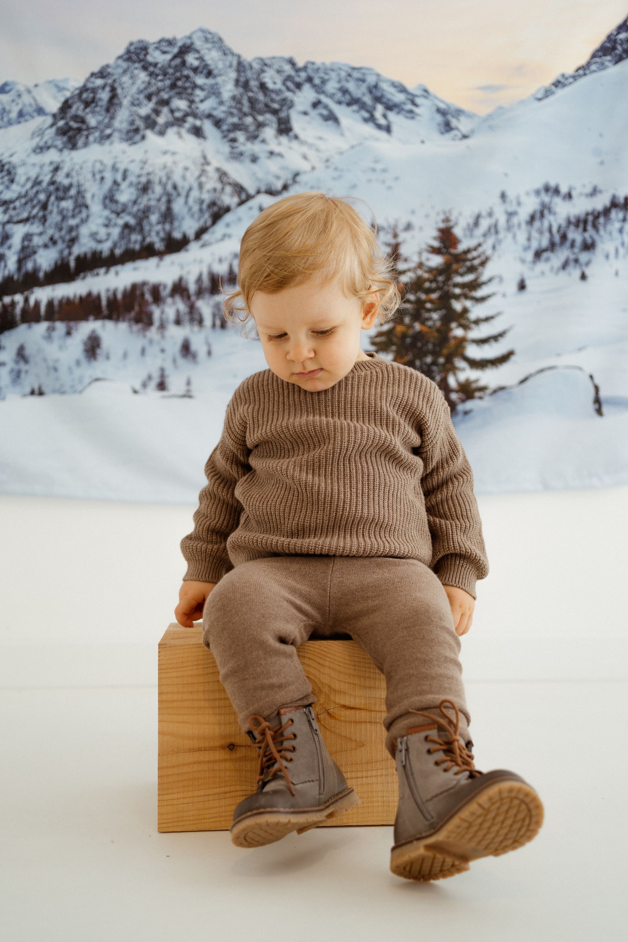 Dziecko siedzi w szarych zimowych butach Emel na tle gór