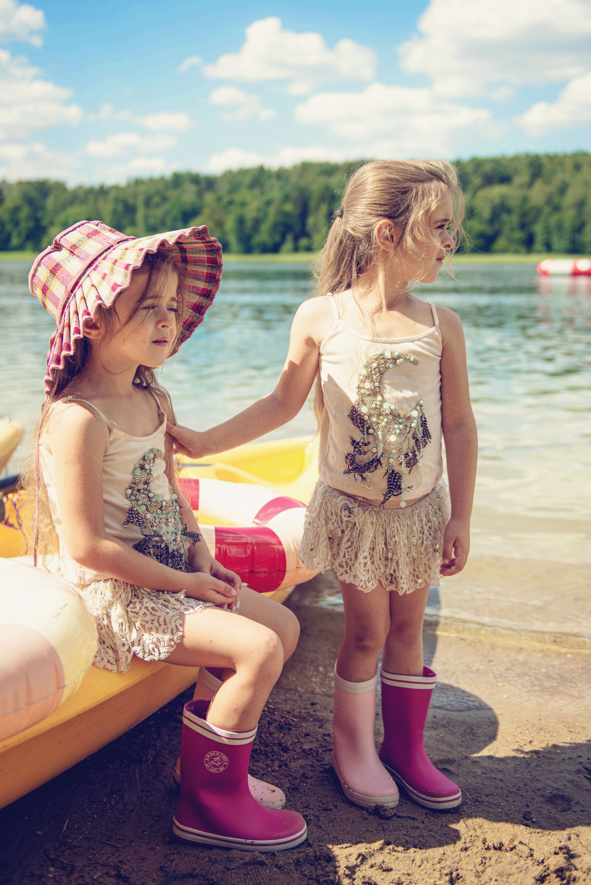 Dziewczynki ubrane w kalosze marki Emel stoją nad jeziorem w piasku