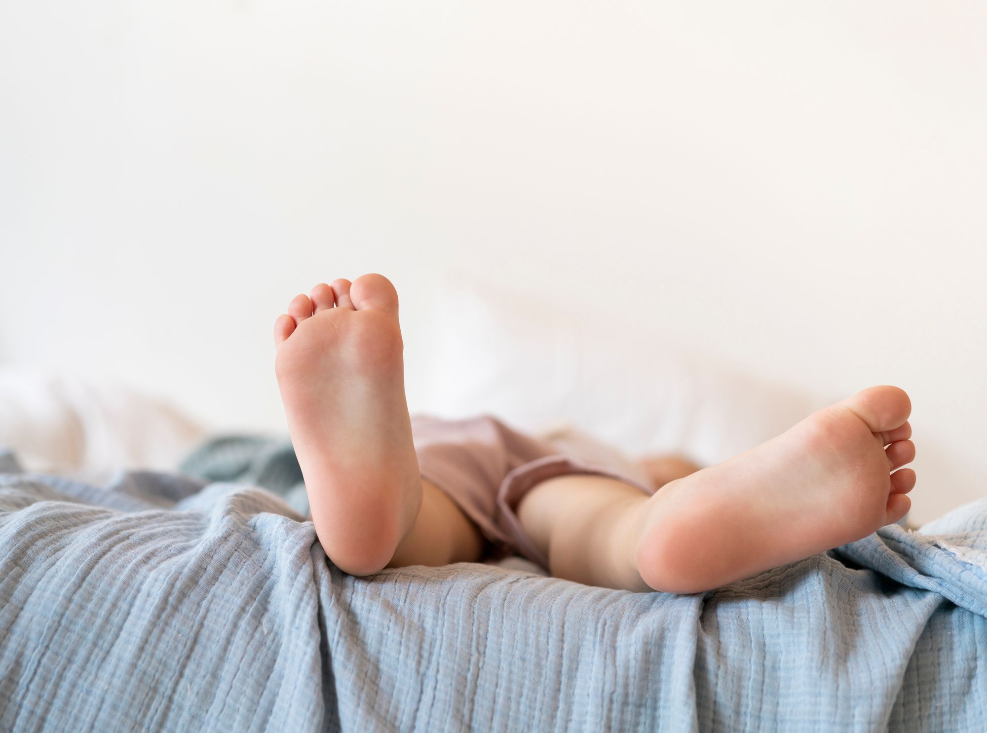 Przybliżenie na dziecięce gołe stopy, dziecko leży na niebieskim kocyku
