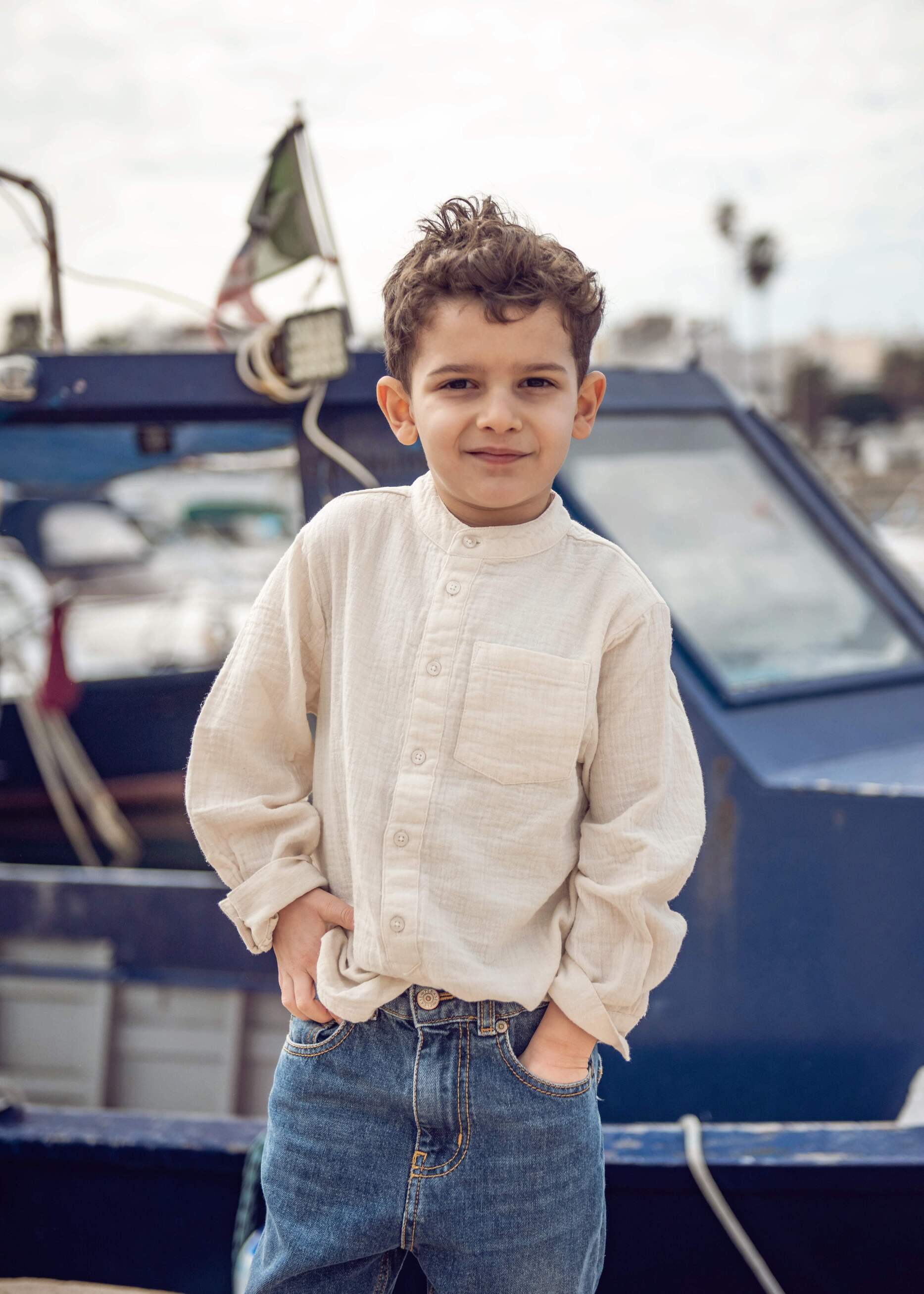 Chłopiec siedzi na krześle w zielonych skórzanych trampkach dziecięcych na trzy rzepy podczas sesji zdjęciowej.