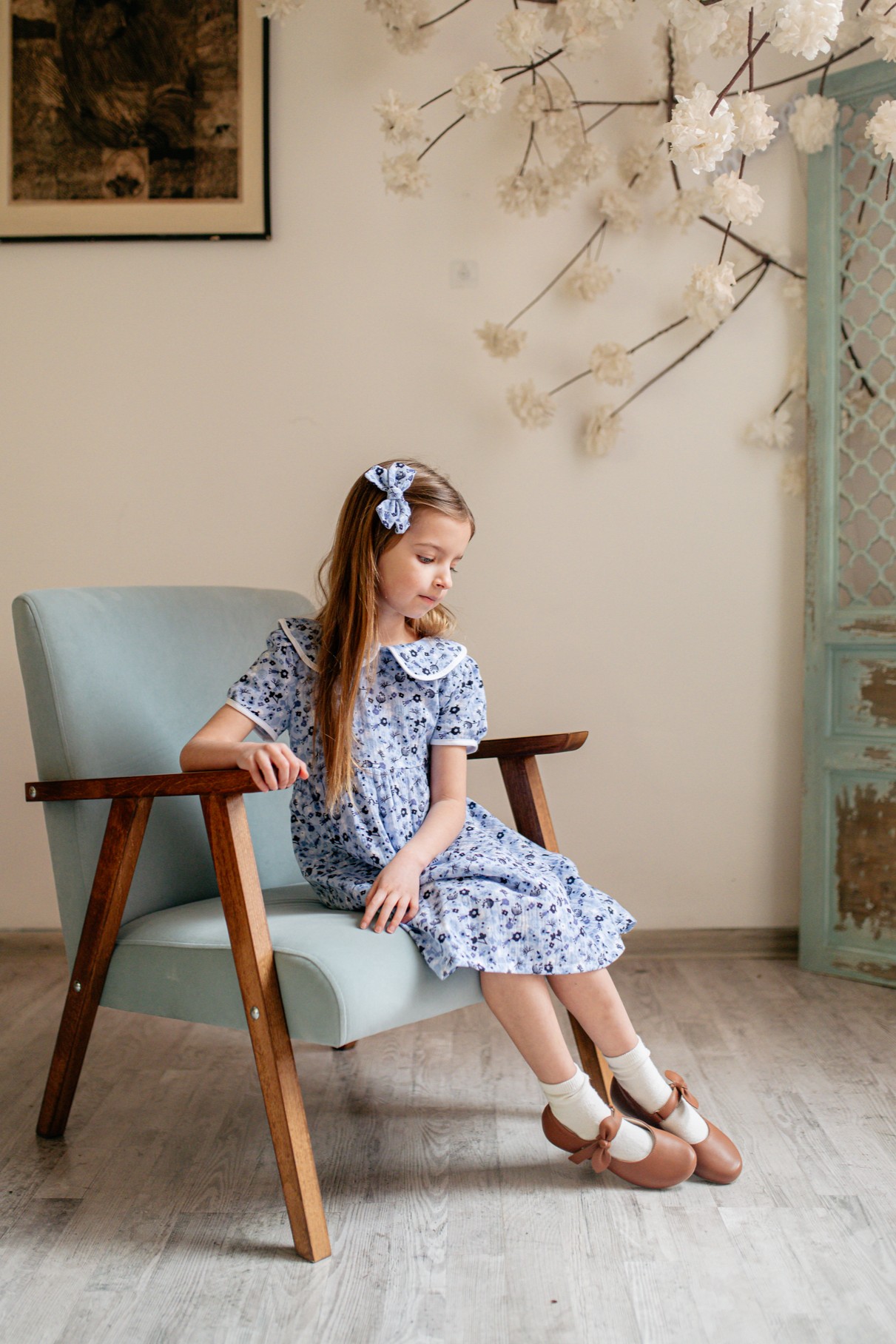 Dziewczynka w zwiewnej sukience pozuje w brązowych, skórzanych balerinkach marki Emel – eleganckich i wygodnych butach idealnych na zakończenie roku szkolnego.