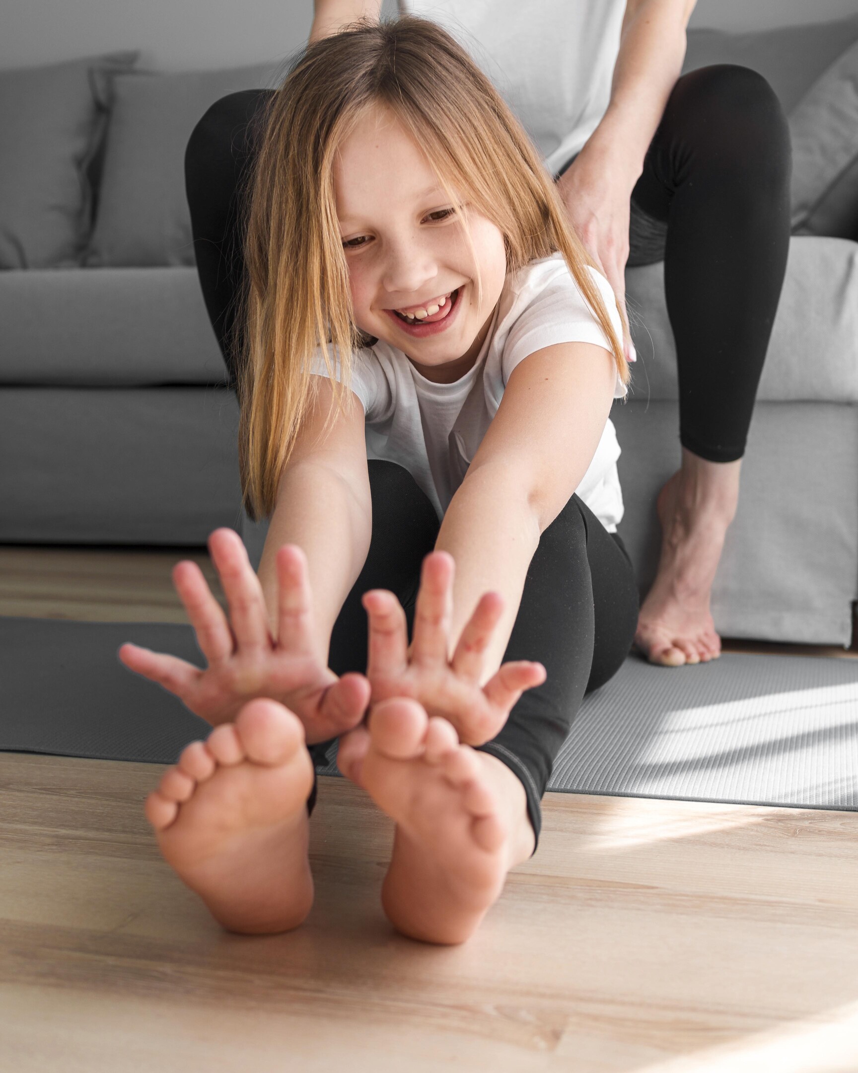 Jak zmierzyć stopy dziecka w domu – wesoła dziewczynka siedzi boso na podłodze, ilustracja do poradnika dla rodziców.