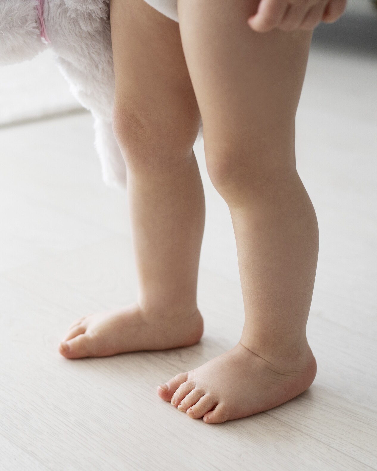 Małe dziecko chodzi boso po podłodze w domu, ucząc się równowagi i prawidłowego ustawienia stóp.